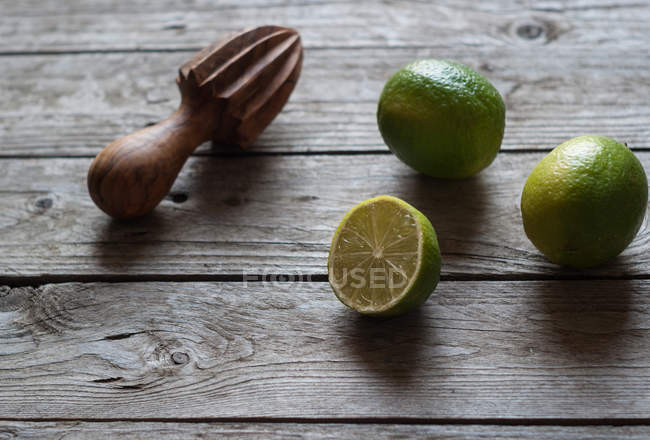 Lime fresco intero e dimezzato con spremiagrumi in legno su legno grigio — Foto stock