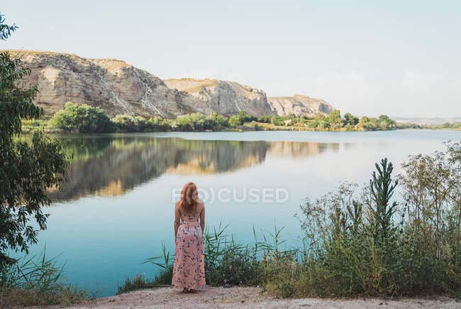 Жінка в довгій літній сукні, стоячи на березі озера — стокове фото