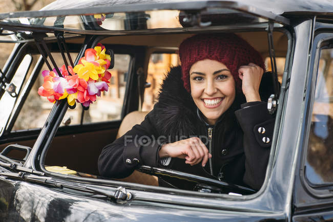 Souriant jeune femme en vêtements chauds assis à l'intérieur de la voiture et en regardant la caméra — Photo de stock