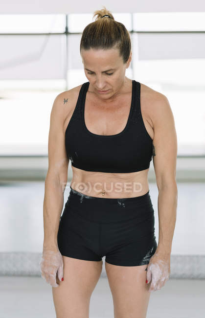 Atleta mulher com as mãos cobertas com giz de pé no ginásio durante o treinamento — Fotografia de Stock