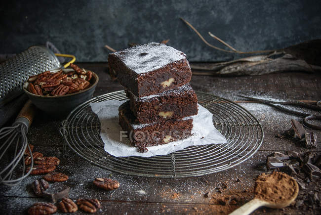 Pedaços de chocolate delicioso brownie no rack de arame com ingredientes na superfície de madeira escura — Fotografia de Stock
