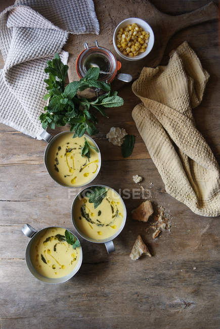 Sopa de creme de milho com coco e pesto em tigelas em mesa de madeira com ingredientes — Fotografia de Stock