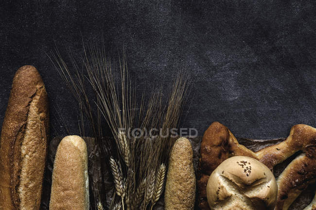 Pani appena sfornati e spighe di grano su superficie nera — Foto stock