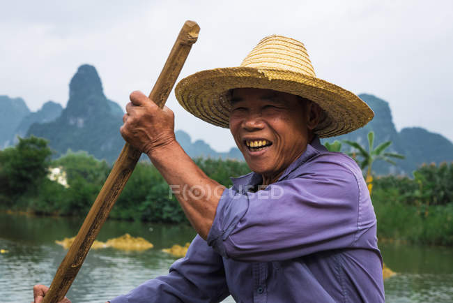 Homem chinês sentado em jangada no rio com montanhas no fundo — Fotografia de Stock
