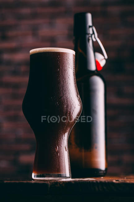 Stout beer in glass and bottle on dark background — Stock Photo