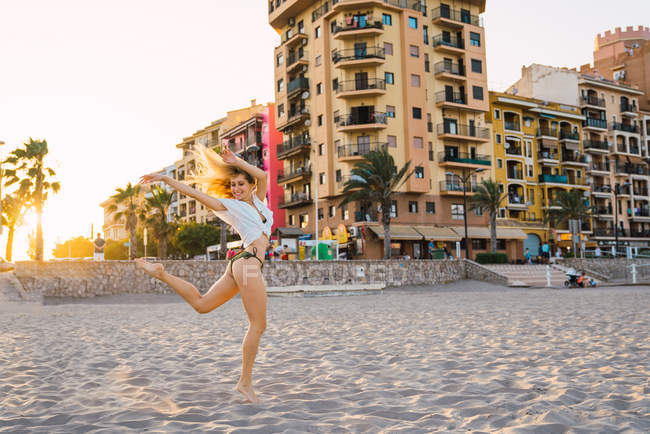 Веселая женщина танцует на одной ноге на пляже на закате — стоковое фото