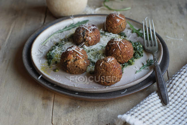 Lentil meatballs garnished with arugula pesto sauce and cheese on plate on wooden table — Stock Photo