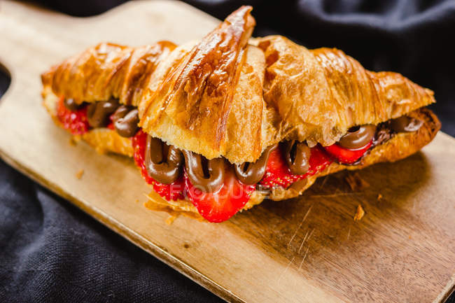 Croissant with chocolate and strawberry on wooden board — Stock Photo