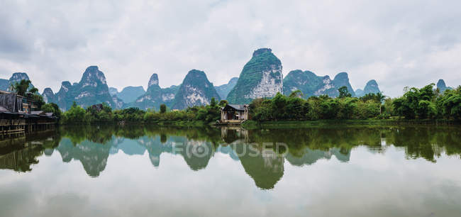 Небольшая рыбацкая деревня на берегу реки Куи Сон и спокойная вода с отраженными горами, Гуанси, Китай — стоковое фото