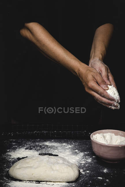 Mãos humanas amassar massa de farinha em mesa no fundo preto — Fotografia de Stock