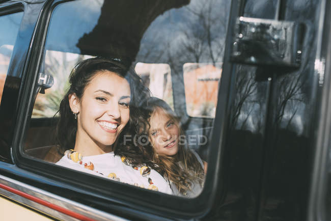 Mujer joven y chica rubia sentada dentro del coche y mirando a la cámara - foto de stock