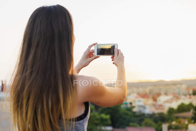 Woman taking picture of town at sunset — Stock Photo