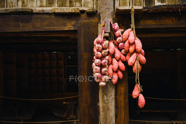 Chinese sweet potatoes and garlic hanging in bunches on wooden wall — Stock Photo