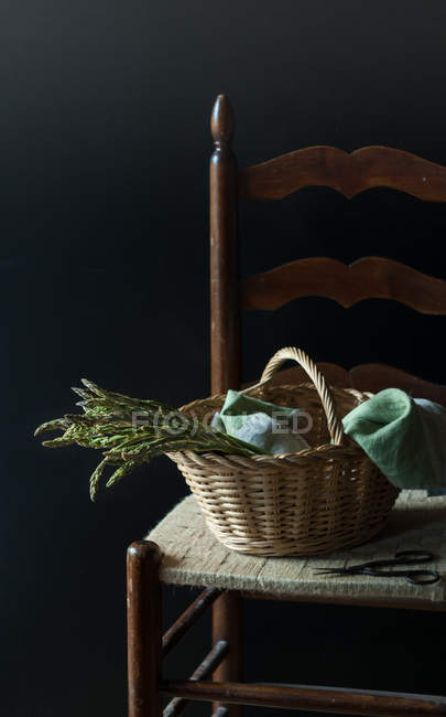 Panier d'asperges vertes fraîches sur chaise sur fond noir — Photo de stock