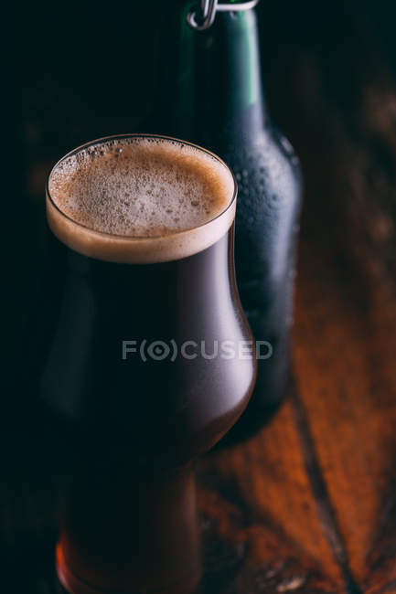 Cerveza en vidrio y botella sobre fondo de madera oscura - foto de stock