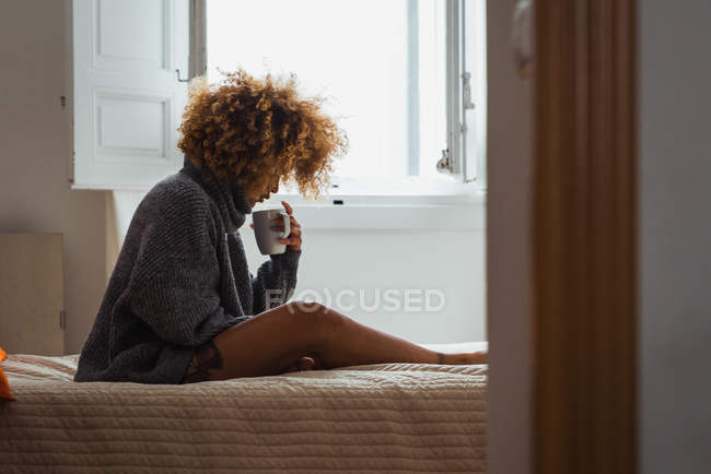 Етнічна жінка розслабляється з кавою і книги на ліжку вдома — стокове фото