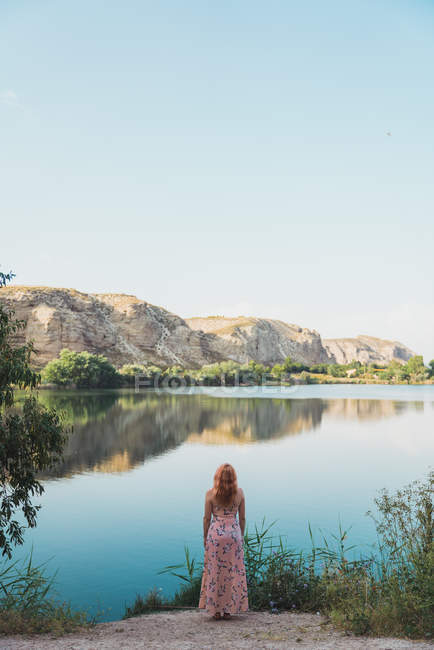 Donna in abito lungo estate in piedi sulla riva del lago — Foto stock