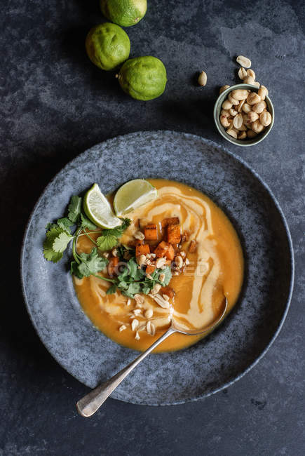 Thai pumpkin soup with limes and peanuts in grey plate on grey surface — Stock Photo