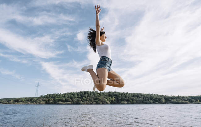 Donna allegra salta vicino al lago. — Foto stock