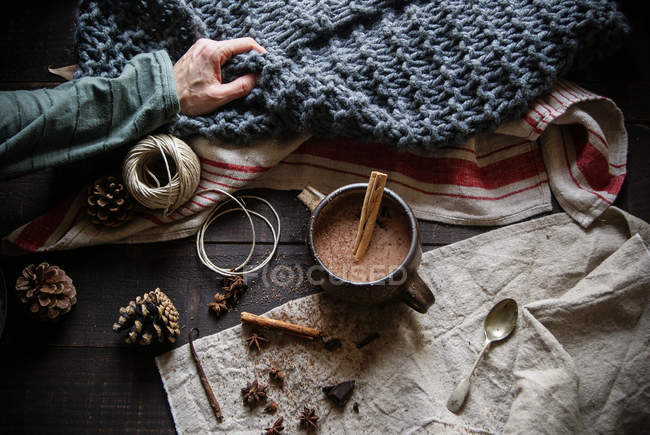 Cioccolata calda con cannella in tazza su sfondo rustico con mano umana — Foto stock