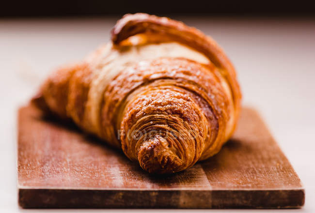 Close-up de delicioso croissant dourado recém-assado com crosta na placa de madeira — Fotografia de Stock