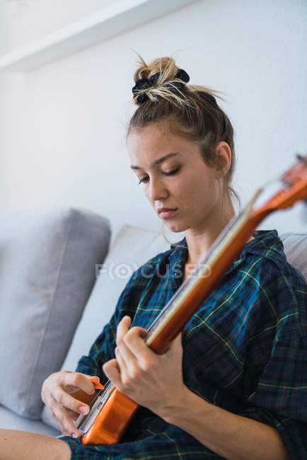 Mujer joven tocando la guitarra en el sofá - foto de stock