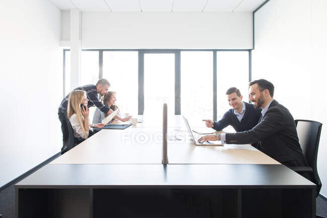 Side view of long table with few groups of coworking people using gadgets and creating new project plan — Stock Photo