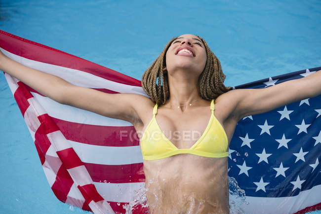 Excited woman standing in swimming pool with American flag — Stock Photo