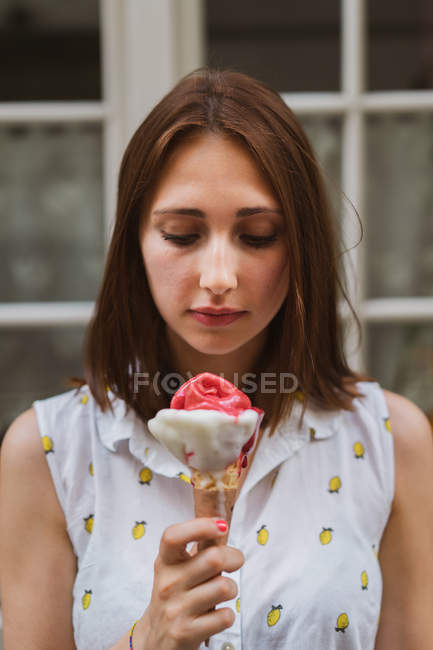 Giovane donna in camicetta fantasia guardando gustoso gelato su sfondo sfocato — Foto stock