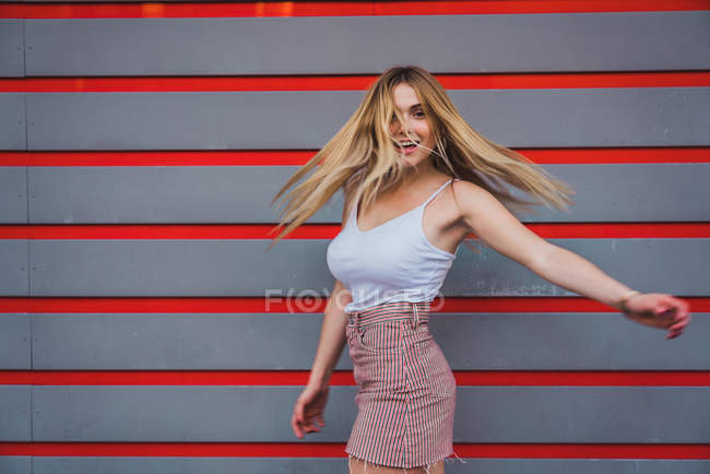 Giovane donna in abito casual ridere mentre in piedi contro la parete a strisce — Foto stock
