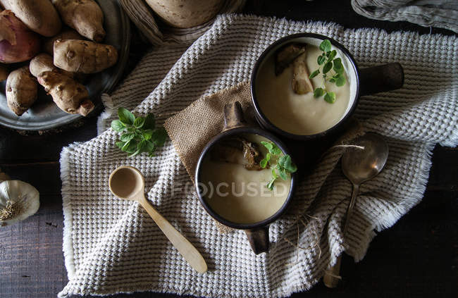 Ciotole di gustosa zuppa di topinambur con ingredienti su tavola rustica di legno — Foto stock
