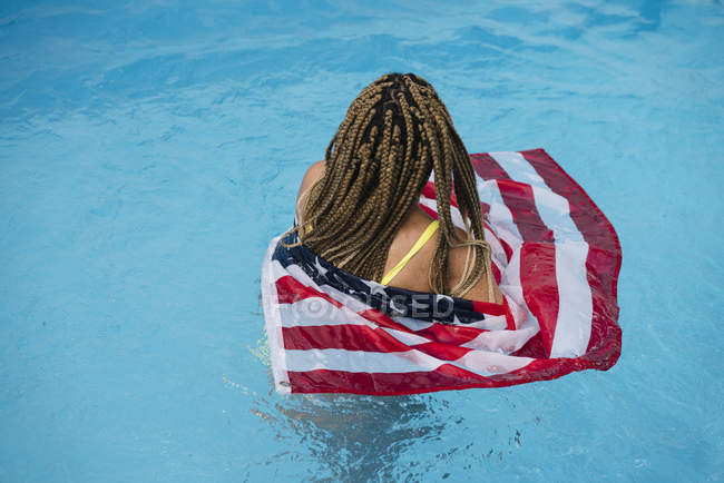 Vue arrière de la femme dans la piscine tenant le drapeau américain — Photo de stock