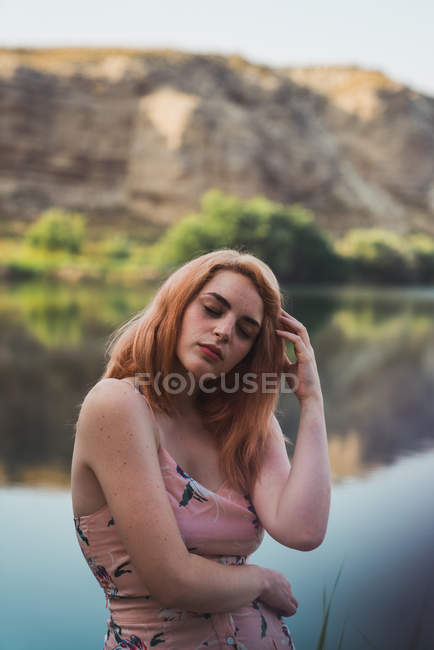 Mulher em vestido de verão em pé na margem do lago com os olhos fechados — Fotografia de Stock