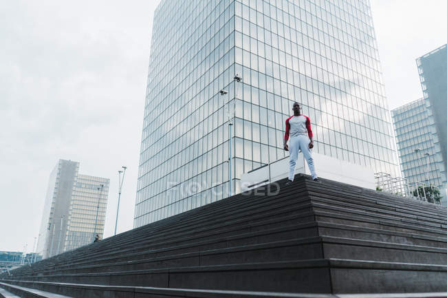 Homme en tenue de sport debout sur les escaliers avec des gratte-ciel en verre modernes sur le fond — Photo de stock