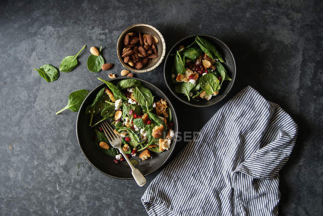 Салат с овощами, сыром и миндалем в мисках на серой поверхности — стоковое фото