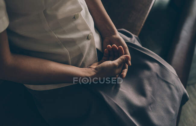 Crop shot from above of woman in simple clothes sitting on bench with hands on knees in devotion — Stock Photo