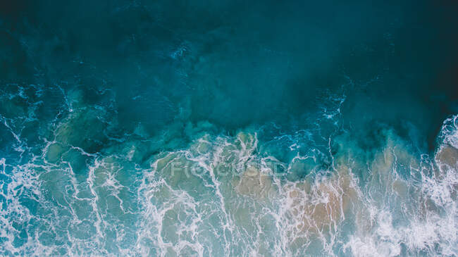 Vista aérea de ondas azuis brilhantes do mar com espuma que rola acima da costa arenosa — Fotografia de Stock
