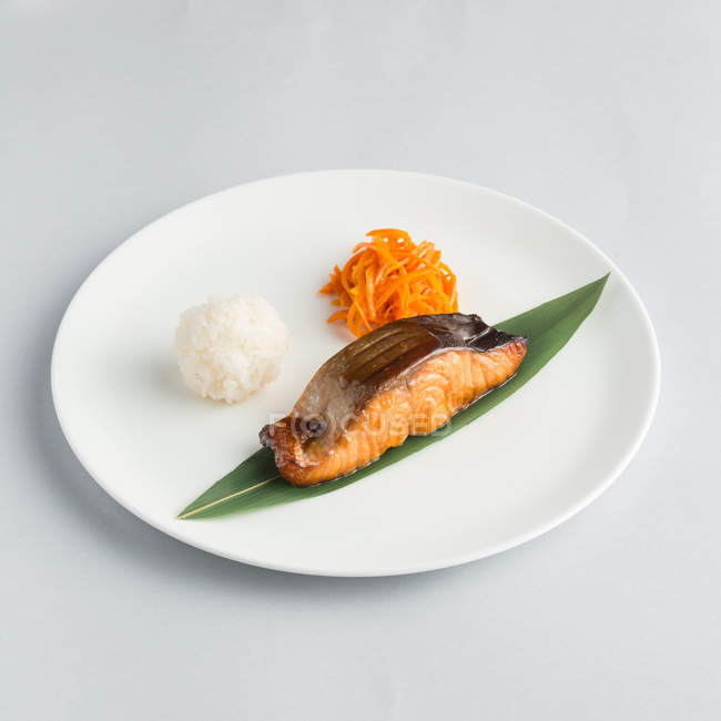 Композиция с жареным лососином и рисовым шариком на белой тарелке — стоковое фото