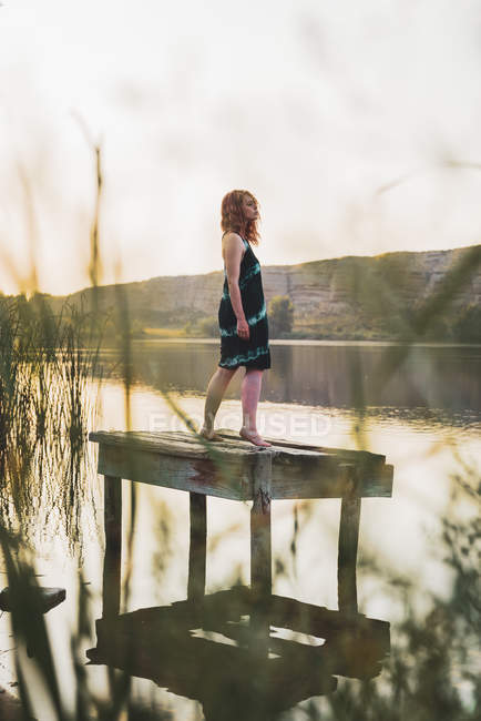 Чуттєва молода жінка стоїть на дерев'яному пірсі на озері — стокове фото