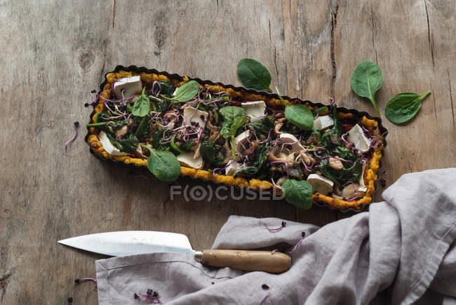 Torta assada com polenta e espinafre coberto com pedaços de queijo crottin em assadeira na mesa de madeira — Fotografia de Stock