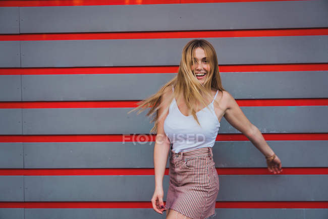 Молода жінка у випадкових спорядження, сміючись стоячи проти смугастий стіни — стокове фото