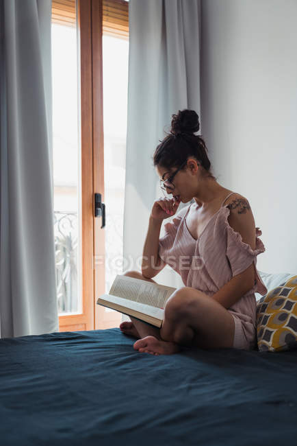 Sensuale bruna donna con libro agghiacciante sul letto — Foto stock