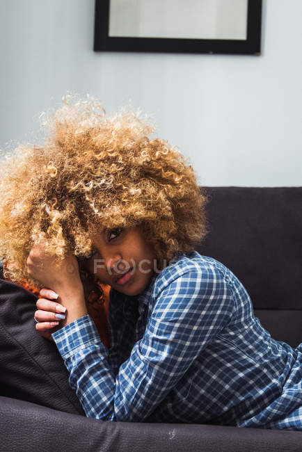 Очаровательная женщина в рубашке, лежащая на диване и смотрящая в камеру — стоковое фото