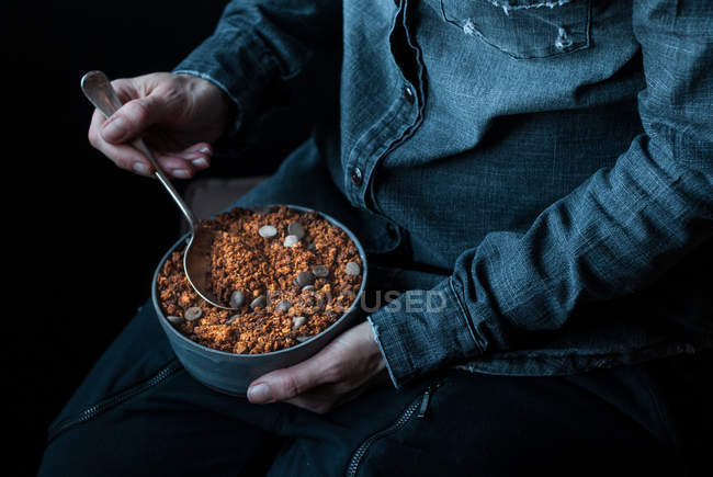 Mãos masculinas segurando tigela de crocante quinoa granola no fundo escuro — Fotografia de Stock