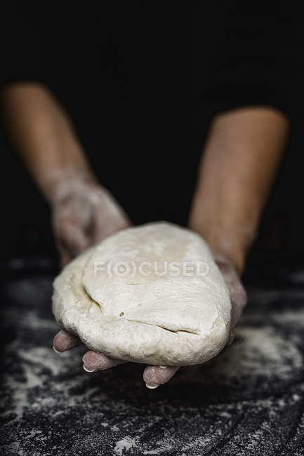 Close-up of human hands holding dough on dark background — Stock Photo