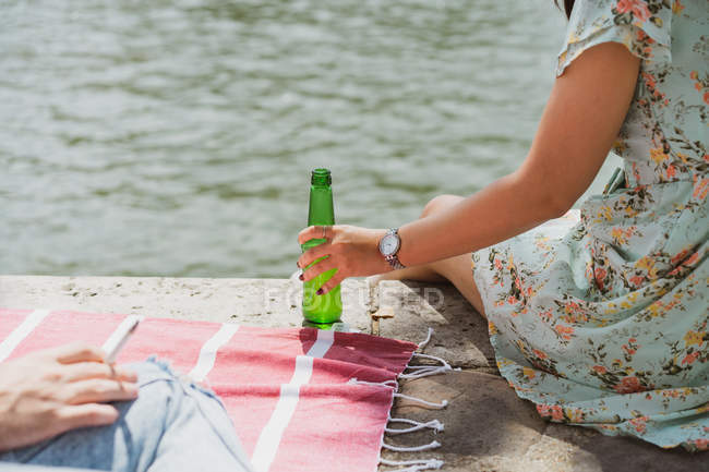 Female hand holding bottle of beer at waterfront — Stock Photo