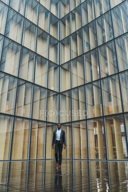 Businessman walking on pavement against modern glass building — Stock Photo