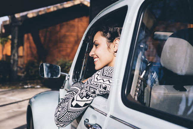 Young woman sitting inside retro car in countryside and looking away — Stock Photo