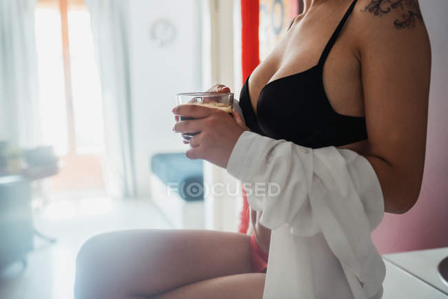 Femme sensuelle en lingerie assise sur le comptoir de la cuisine avec une tasse de café — Photo de stock