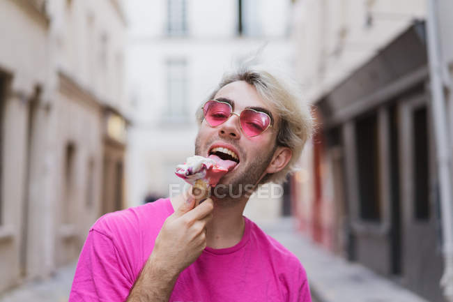 Stylish man in pink t-shirt and heart-shaped sunglasses eating ice-cream on street — Stock Photo